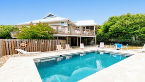 Ein zweistöckiges Haus mit Swimmingpool, einer Holzterrasse und Gartenmöbeln.