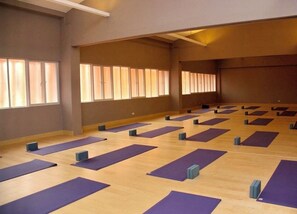 Et rummeligt værelse med flere yogamåtter udlagt på gulvet, store vinduer og højt til loftet.