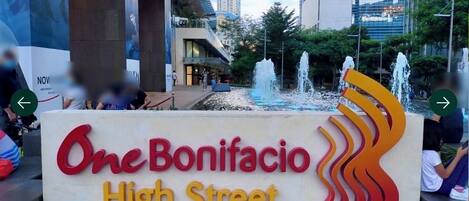 A sign for One Bonifacio High Street with a modern design and a water feature in the background.