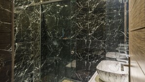Ein modernes Badezimmer mit einer gläsernen Dusche, Marmorwänden und einem Waschbecken aus Marmor.
