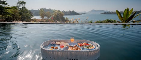 A floating dining setup with a basket containing food and drinks, surrounded by calm water and a scenic view of a lake and mountains.