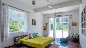A bedroom with a bed, a window, a ceiling fan, and a view of greenery outside.
