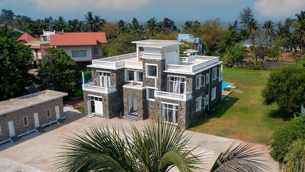 A multi-story house with a stone facade, multiple balconies, and a swimming pool.
