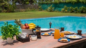 A breakfast setup by a pool with fruits, coffee, and drinks.