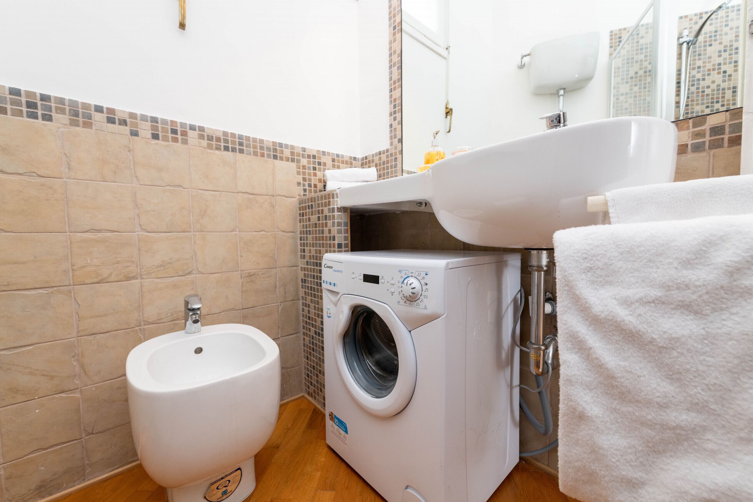 A bathroom with a bidet, a washing machine, and a sink.