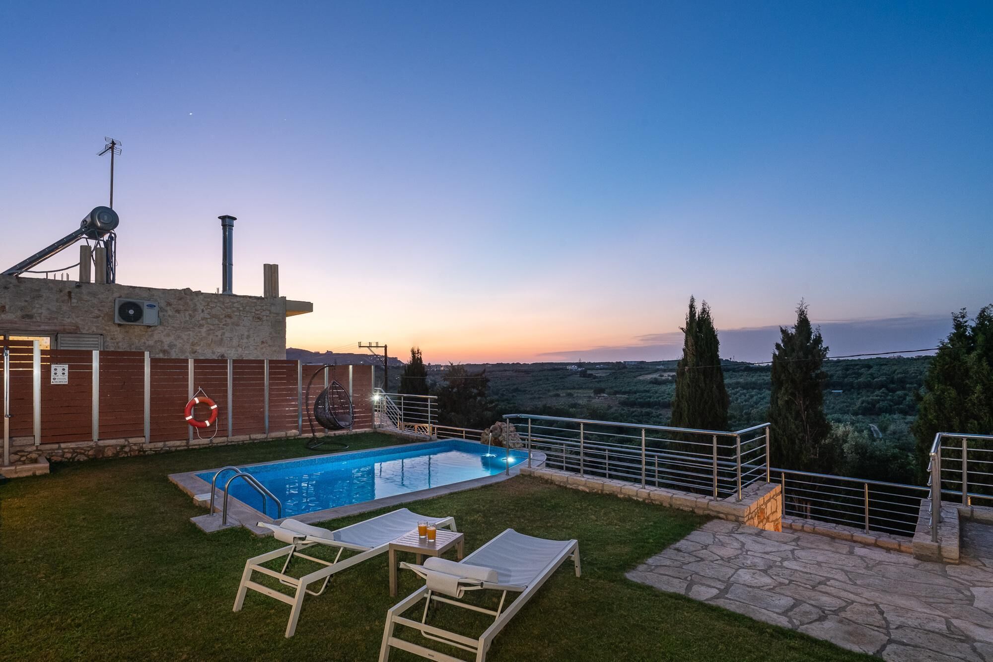 A swimming pool with lounge chairs and a stone pathway, surrounded by a stone wall and a view of the countryside.