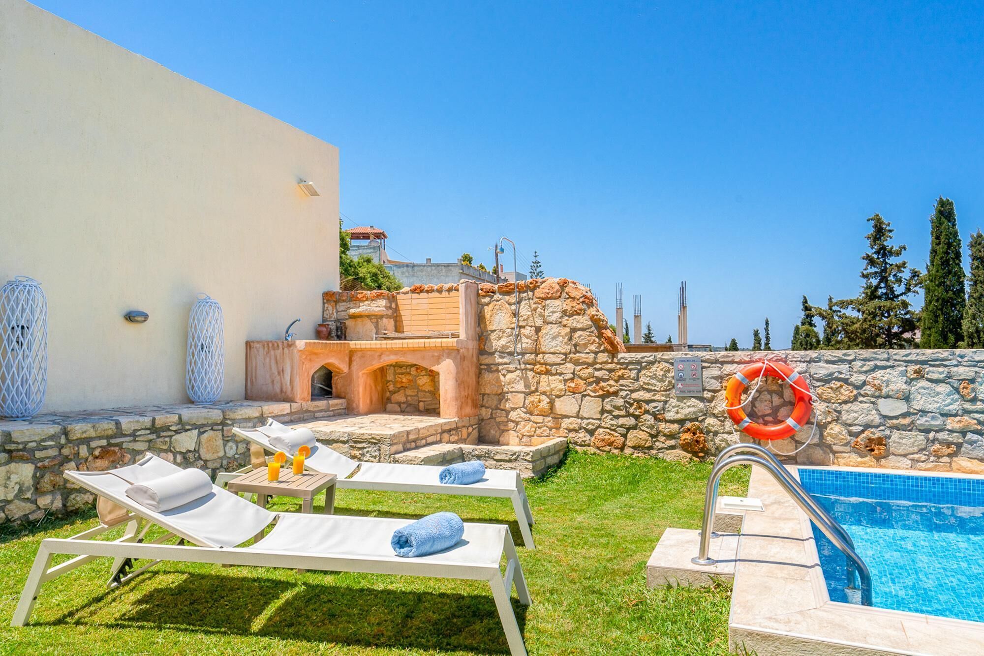 A poolside area with lounge chairs, a stone wall, and a clear blue sky.