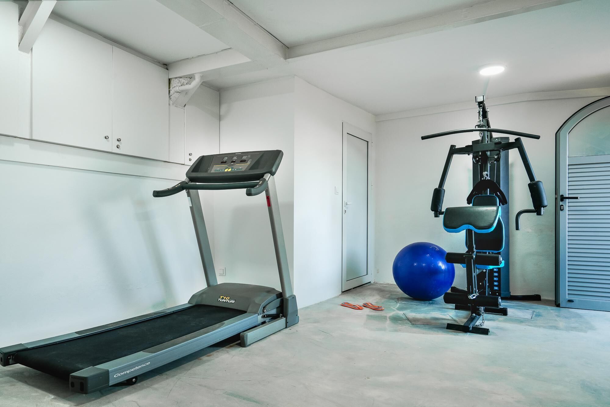 Ett gym med ett löpband, en styrketräningsmaskin och en blå träningsboll.