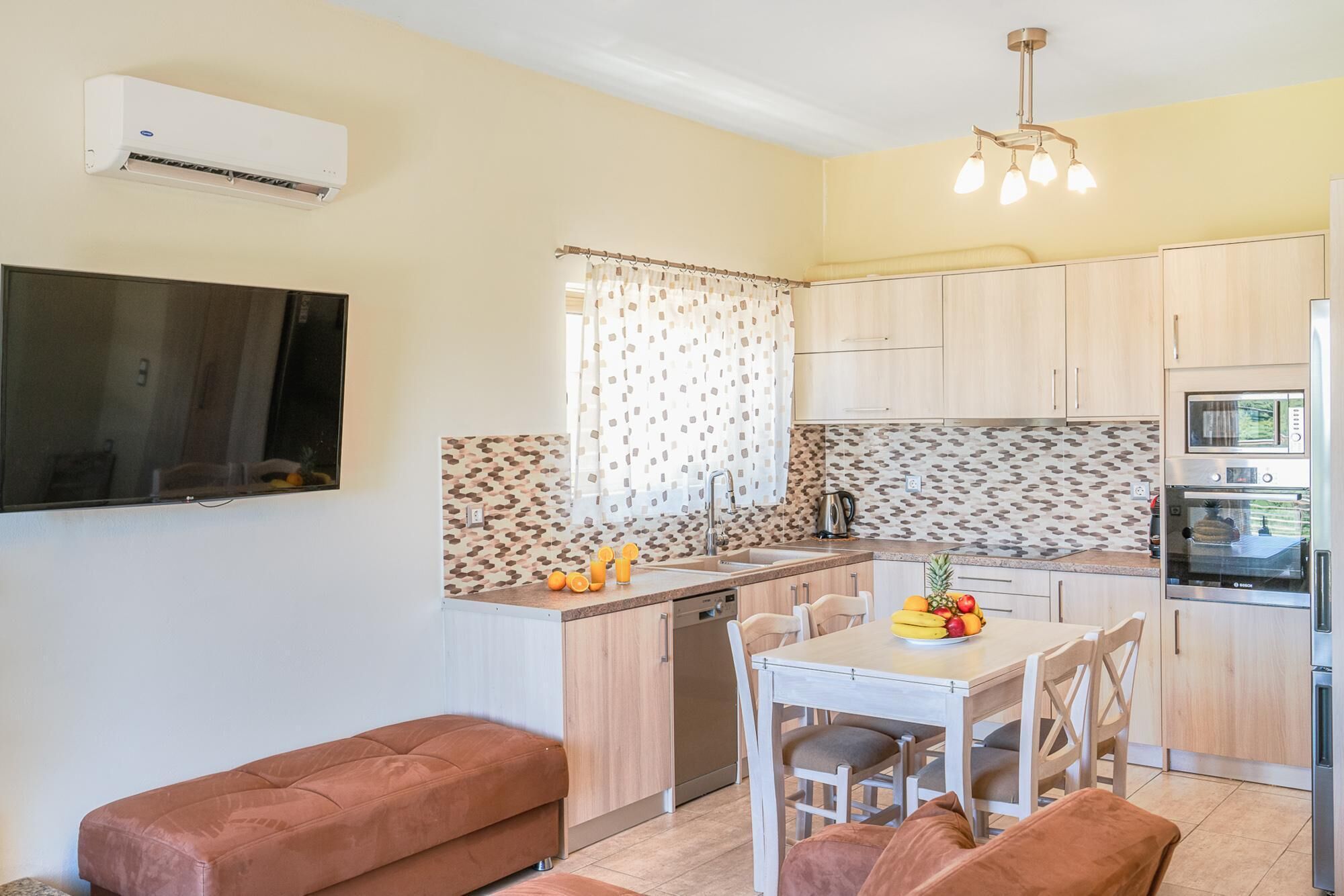 Cocina compacta con comedor, horno empotrado y un televisor de pantalla plana en la pared.