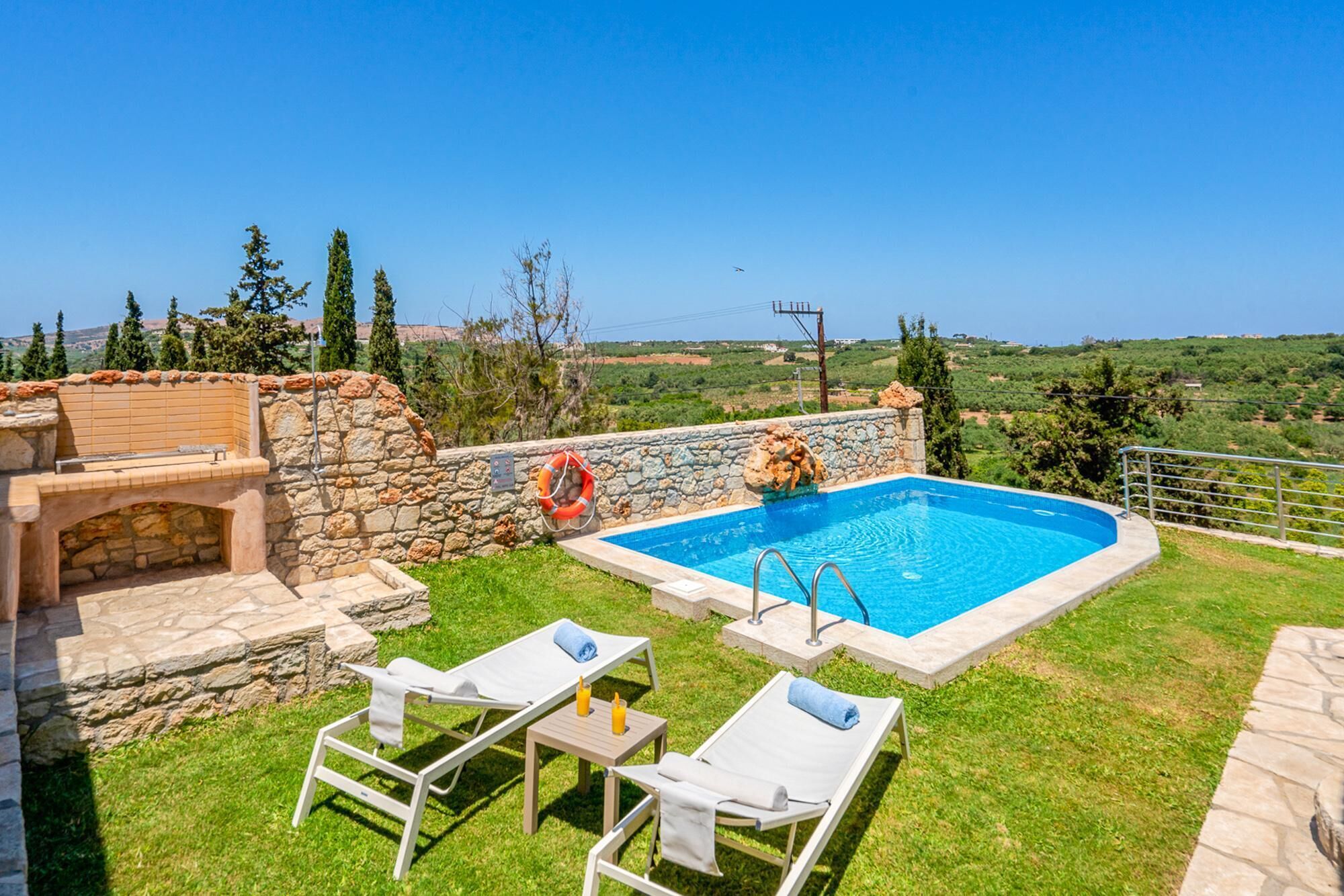 A swimming pool with a stone wall, two lounge chairs, and a lifebuoy.