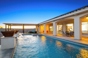 A swimming pool with a patio area, outdoor seating, and a view of the sunset.