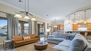 Ein geräumiges Wohnzimmer mit einer großen Couch, einem Couchtisch und einem Essbereich, wobei im Hintergrund eine Küche zu sehen ist.