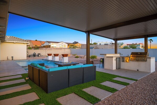 A modern outdoor patio with a pool, a built-in barbecue, and a seating area.