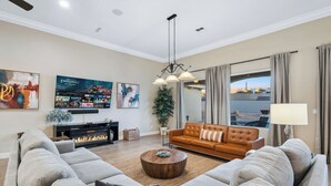 Ein Wohnzimmer mit einem großen Flachbildfernseher, einem Kamin, einem braunen Ledersofa und einem großen Fenster mit Vorhängen.