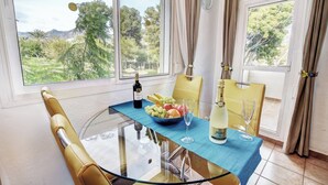 A dining area with a glass table, yellow chairs, a bowl of fruit, wine glasses, and a bottle of champagne.