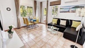 A modern living room with a black sofa, yellow chairs, a glass coffee table, and a dining area with a table and chairs.