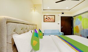A hotel room with a large bed, a headboard, a blue sofa, a door, and a painting on the wall.