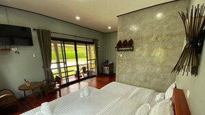 A hotel room with a large bed, a TV, a dining area with a table and chairs, and a view through the glass doors. - Pruksa View Homestay (Nam Nao)