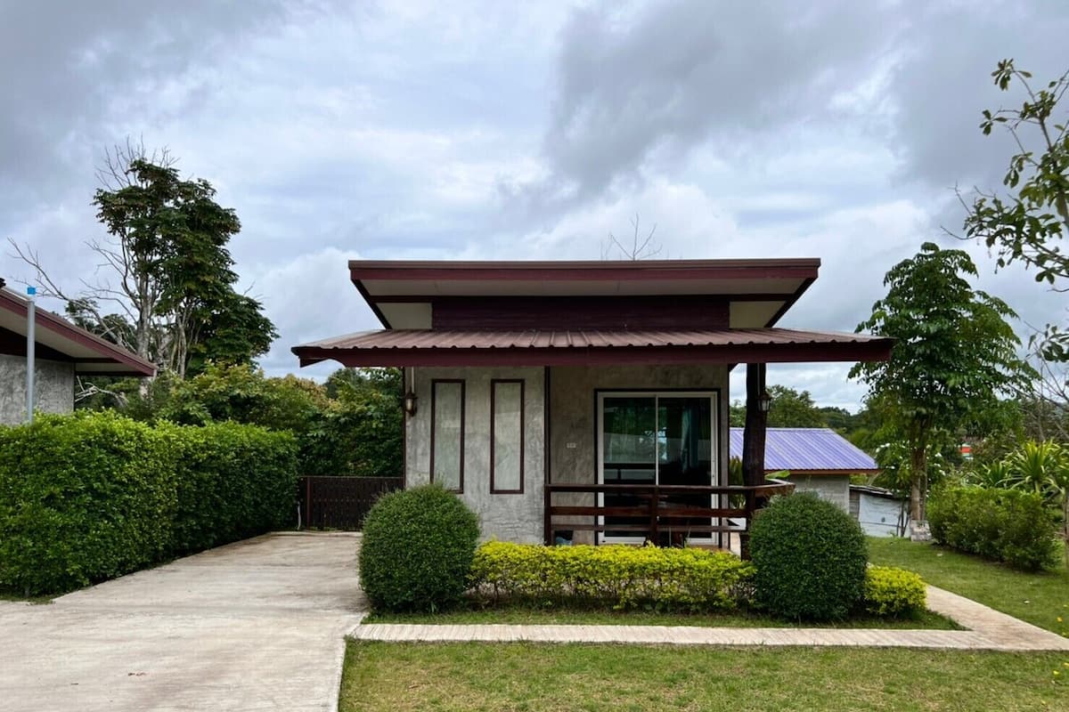 Uma casa moderna com varanda coberta, caminho de concreto e sebes bem cuidadas.