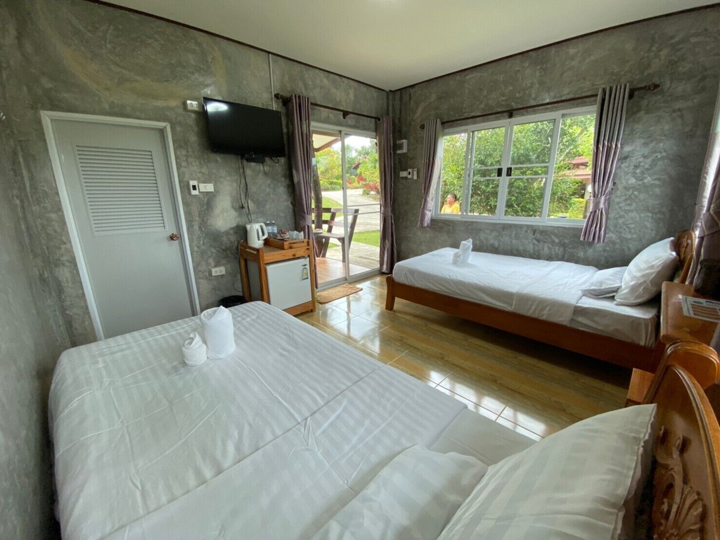 Habitación de hotel con dos camas, televisión, refrigerador pequeño y ventana con cortinas.