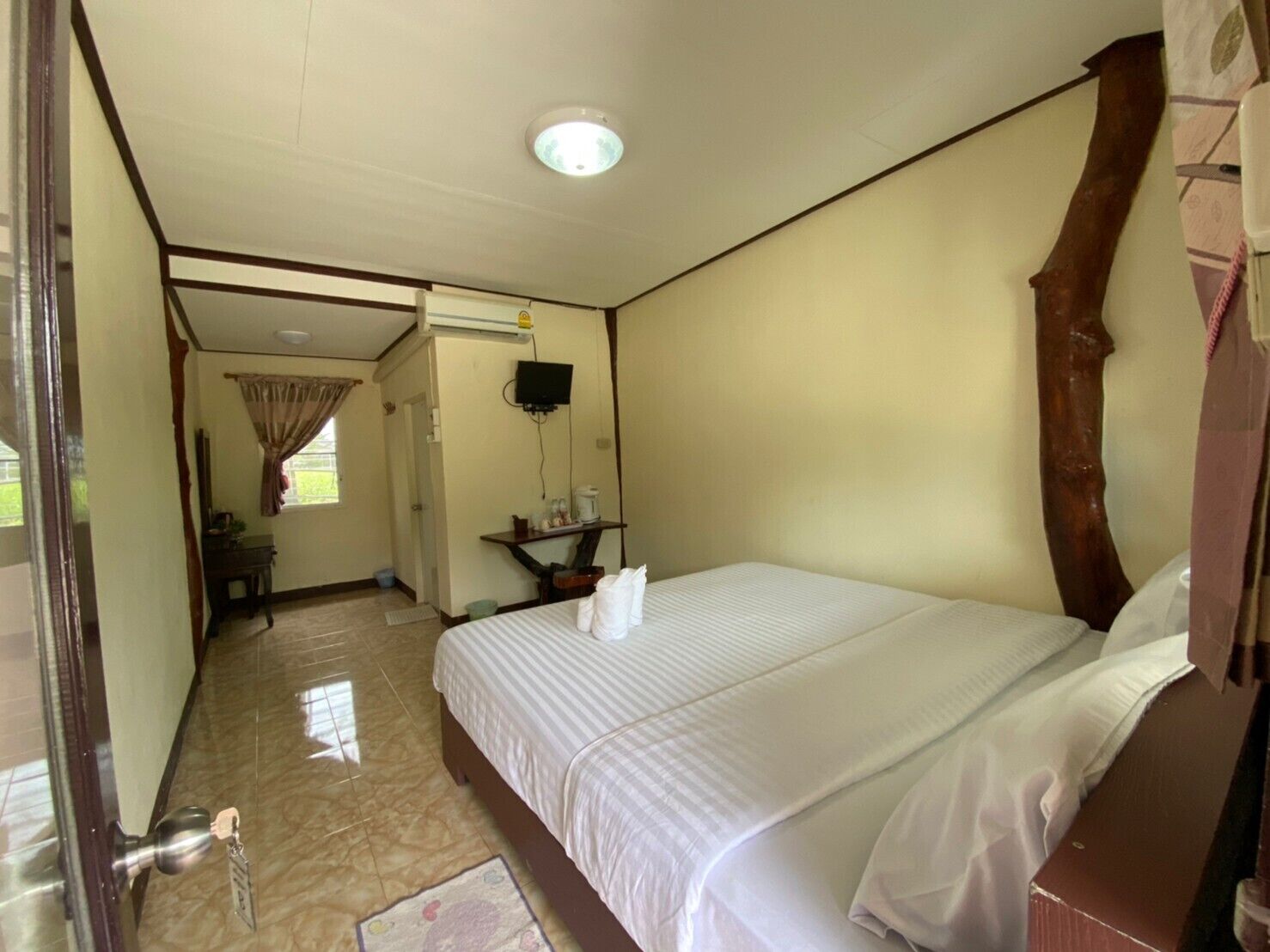 A hotel room with a large bed, a television, a desk, and a window with curtains.