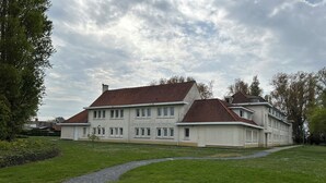 A large, two-story house with a red-tiled roof and a well-maintained lawn. - Chouette Appartement 5 Personnes (De Haan)