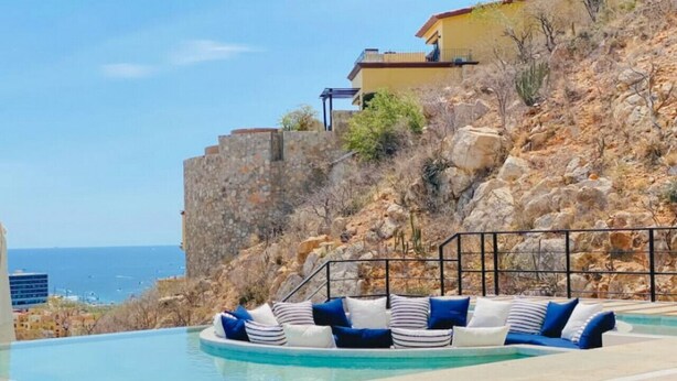 Ein Poolbereich mit einer Steinmauer, eine Lounge mit gestreiften Kissen und Meerblick.