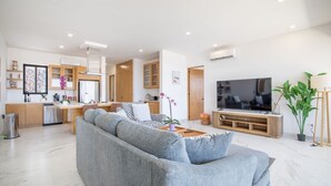 Ein modernes Wohnzimmer mit einem grauen Sofa, einem Fernseher und einer Küche im Hintergrund.