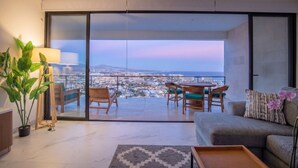 Ein modernes Wohnzimmer mit einer Couch, einem Esstisch, Stühlen und einer großen Glasschiebetür, die auf einen Balkon mit Blick auf die Stadt führt.