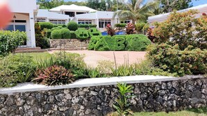 A modern building with a stone retaining wall, well-maintained landscaping, and a clear view of the surrounding area. - The Gabayan Riviera (Lazi)