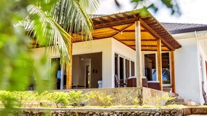 A modern house with a covered porch, a stone retaining wall, and a palm tree in the foreground. - The Gabayan Riviera (Lazi)
