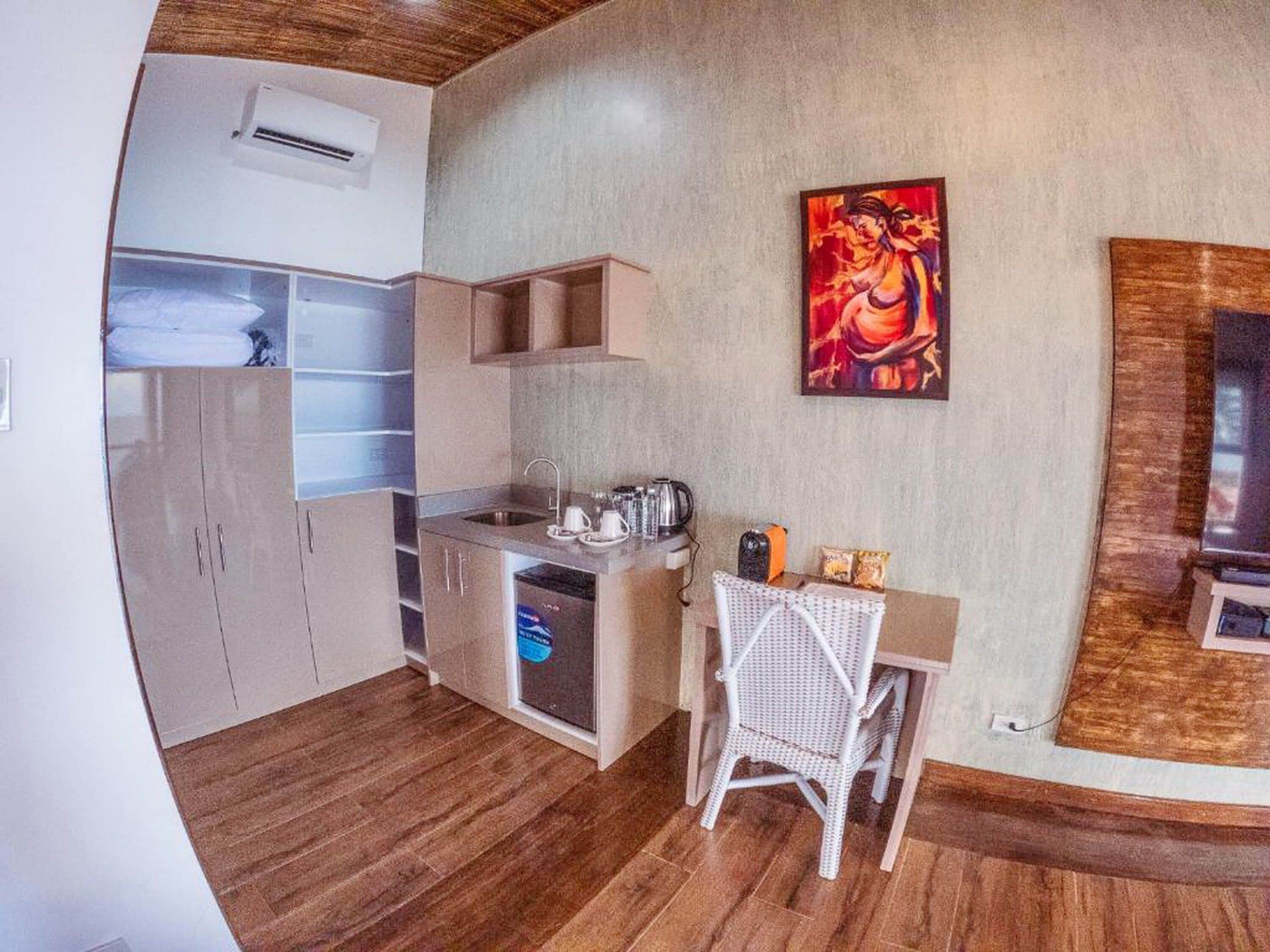A compact kitchen with a sink, a small dining area with a chair, and a painting on the wall.
