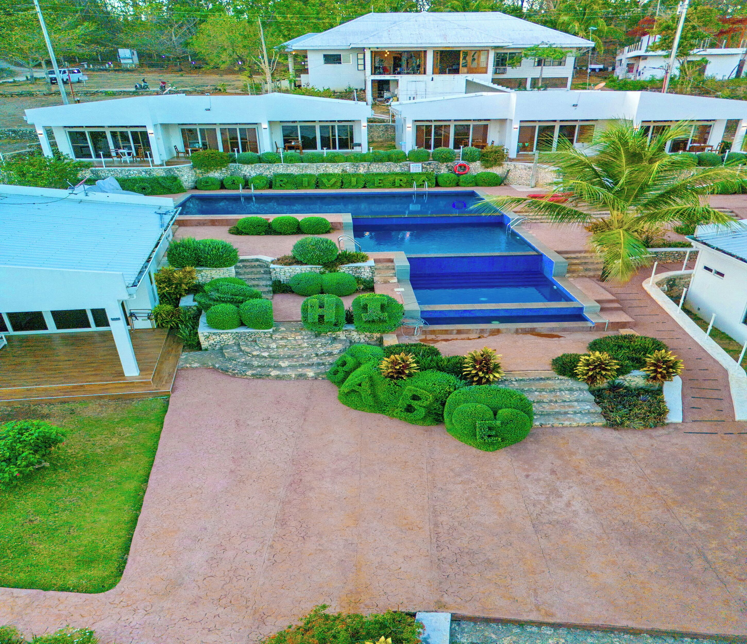A modern building with a swimming pool, surrounded by well-maintained gardens and a stone pathway.
