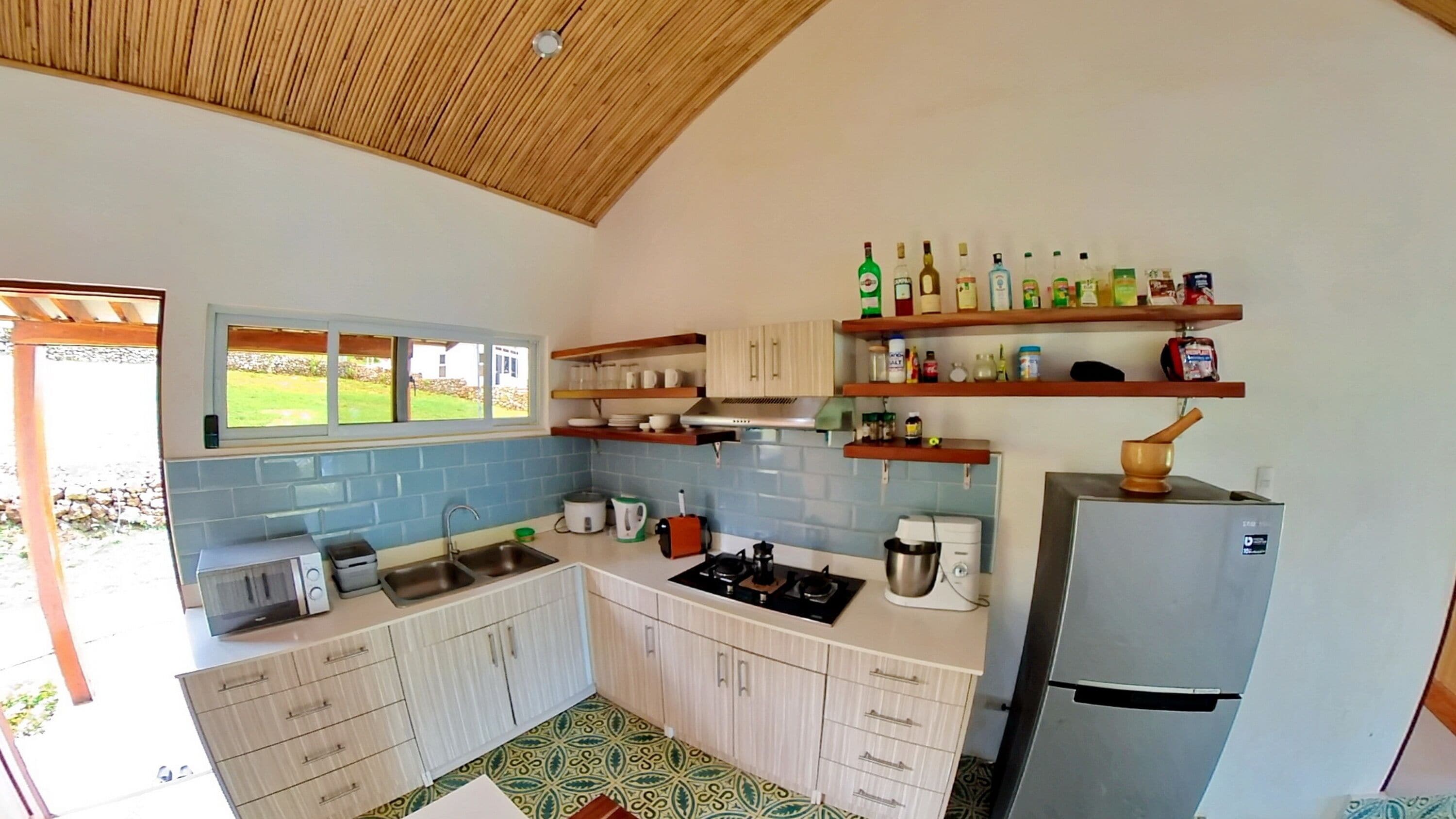 A compact kitchen with white cabinets, a built-in stove, a sink, and a refrigerator. There are shelves above the counter holding various kitchen items.