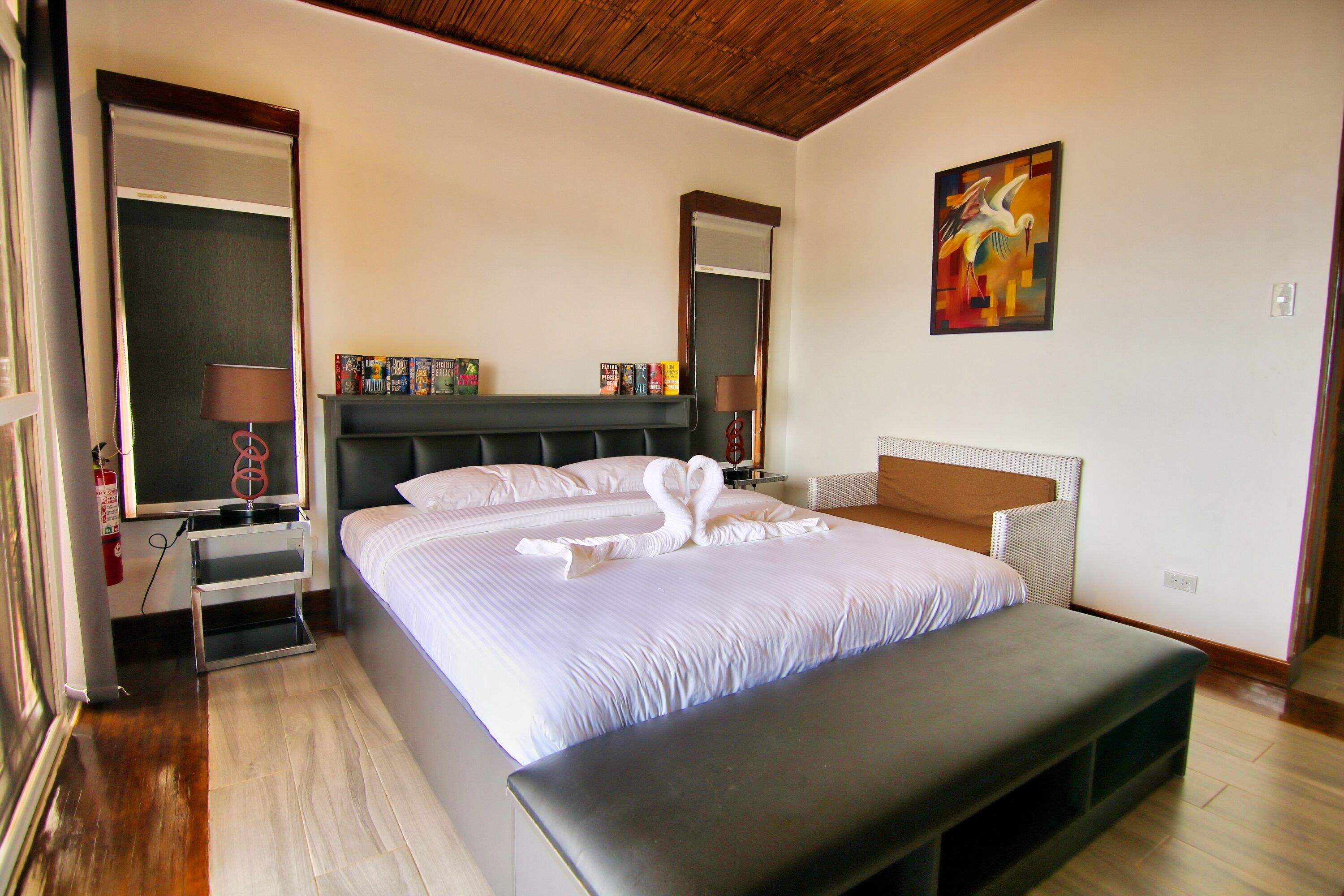 A hotel room with a large bed, bedside tables, a bench, a painting, and a bookshelf.