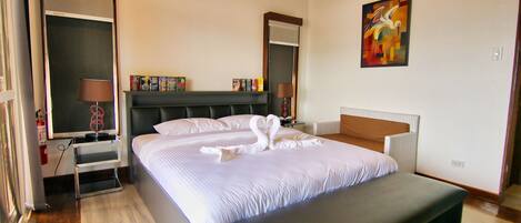 A hotel room with a large bed, bedside tables, a bench, a painting, and a bookshelf.