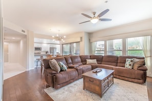 A spacious living room with a large sectional sofa, a wooden coffee table, and a ceiling fan.