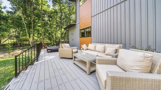 Een terras met rieten meubilair, een houten tafel en een metalen reling.