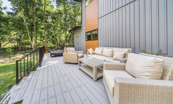 Eine Terrasse mit Korbmöbeln, einem Holztisch und einem Metallgeländer.