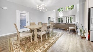 Een moderne keuken met een ingebouwde oven, een eethoek met een houten tafel en stoelen, en een groot raam dat zorgt voor veel daglicht.