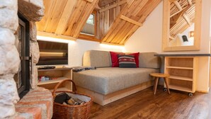 Un acogedor dormitorio en el ático con techo de madera, un sofá con cojines, un televisor, una mesita y una cesta de leña.