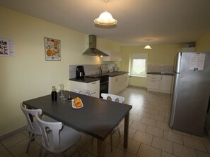 A compact kitchen with a dining table, chairs, a refrigerator, and a window. - Spacious Family-Friendly Cottage with Large Terrace, Garden, and Easy Access to Ski and Lake Activities (Docelles)