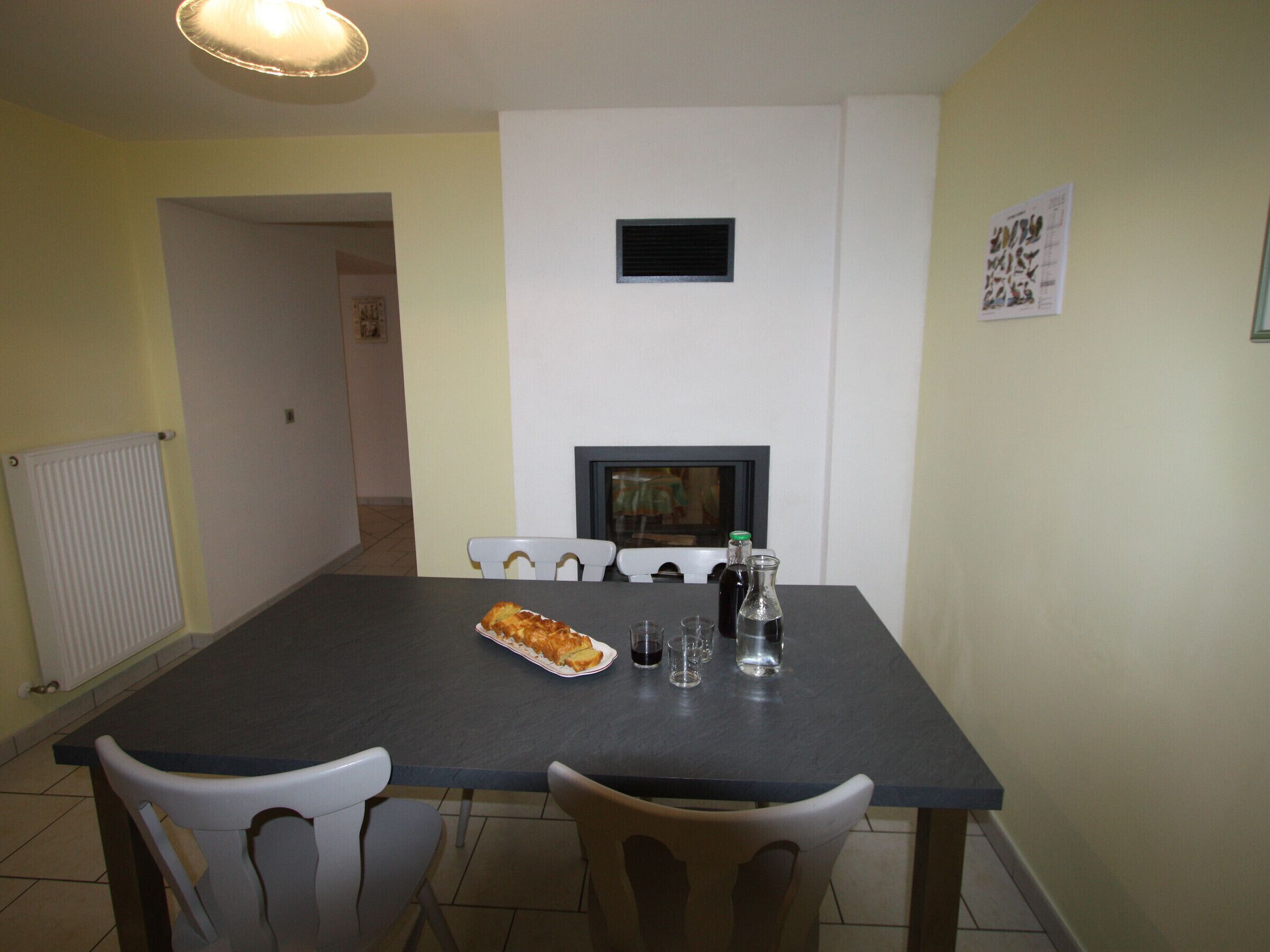 Un comedor con una mesa, sillas, un radiador, una chimenea y un cuadro en la pared.