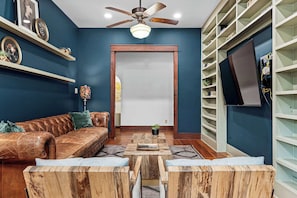 A living room with a leather sofa, wooden coffee table, and a ceiling fan. - Grit&Grace Ranch - Private Resort Style Pool & Spa (Austin)