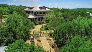 A large house surrounded by dense forest, with a well-maintained garden and a clear sky. - Grit&Grace Ranch - Private Resort Style Pool & Spa (Austin)