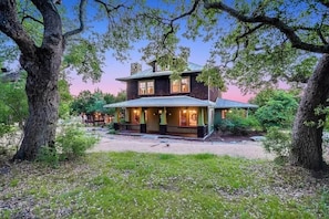 A two-story house with a porch, surrounded by trees. - Grit&Grace Ranch - Private Resort Style Pool & Spa (Austin)