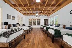 A room with wooden floors, a ceiling fan, and a large window. - Grit&Grace Ranch - Private Resort Style Pool & Spa (Austin)