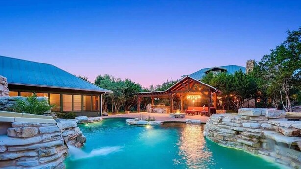 A resort with a swimming pool, stone walls, and a wooden structure. - Grit&Grace Ranch - Private Resort Style Pool & Spa (Austin)