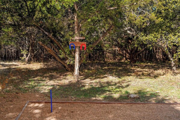 A tree with a sign indicating a horseshoe area. - Grit&Grace Ranch - Private Resort Style Pool & Spa (Austin)