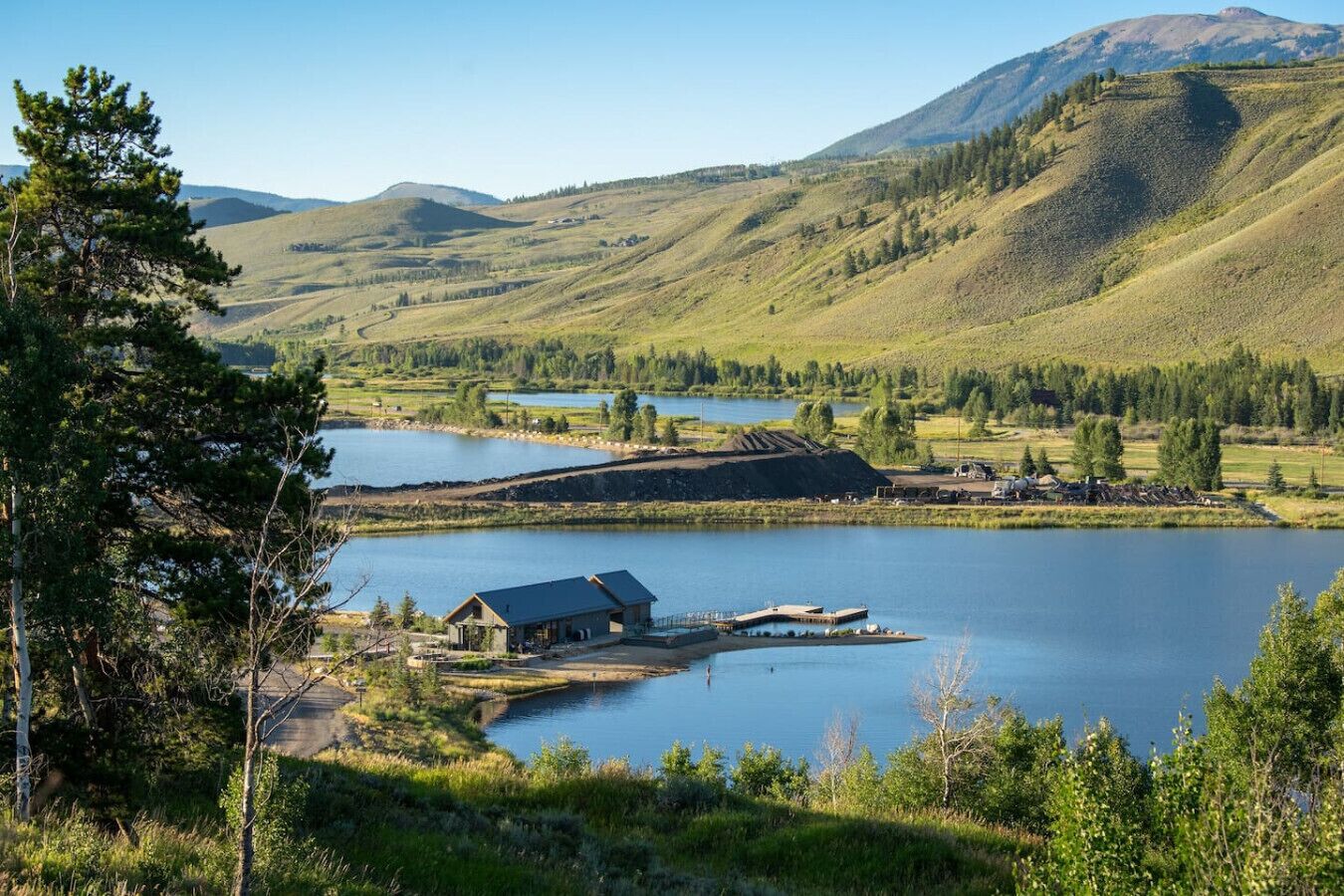 A lakeside cabin with a dock, surrounded by hills and trees.
